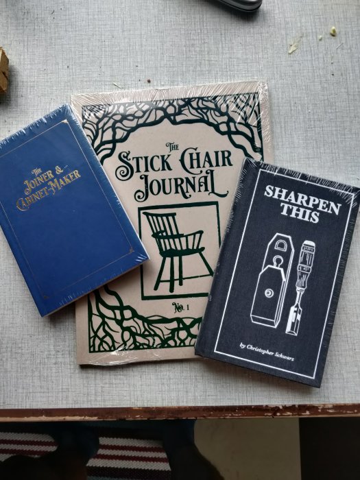 Tre böcker om hantverk; "The Joiner & Cabinet Maker", "The Stick Chair Journal", och "Sharpen This" på ett bord.