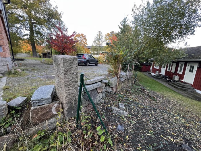 Stenmur vid hus med höstslingrande växter och röda lövträd i bakgrunden.