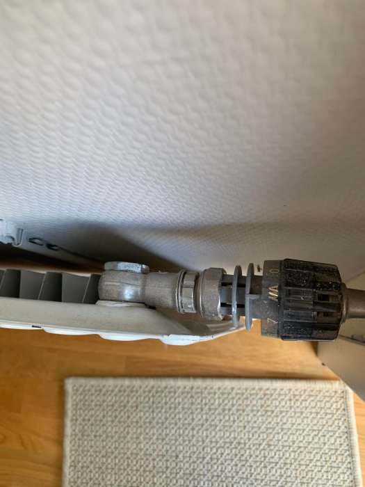 Radiatorkoppling och termostatventil synliga under en fönsterbräda.