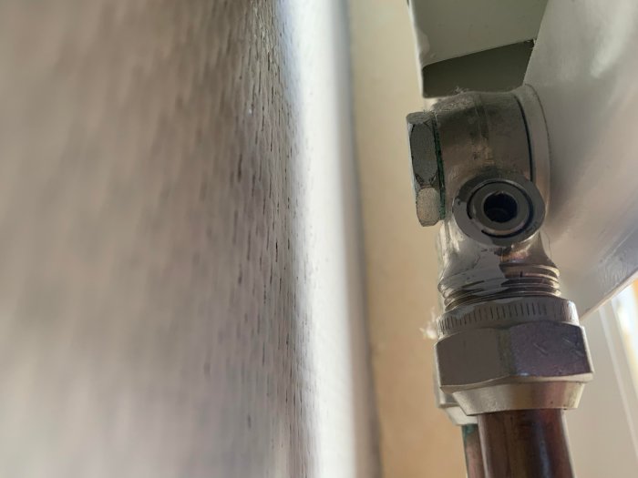 Närbild av en avstängd radiatorventil och kopparledning mot en vit vägg.