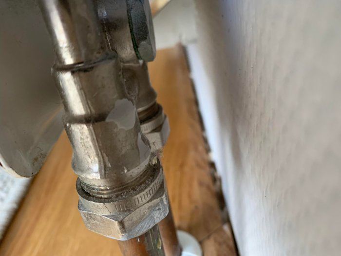 Närbild av ett metalliskt rörkoppling med tecken på vattenläckage och korrosion.