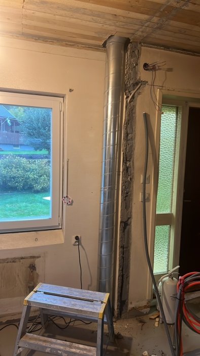 Ventilationsrör installerade upp längs en vägg i en rum under renovering, med verktyg och byggmaterial synliga.