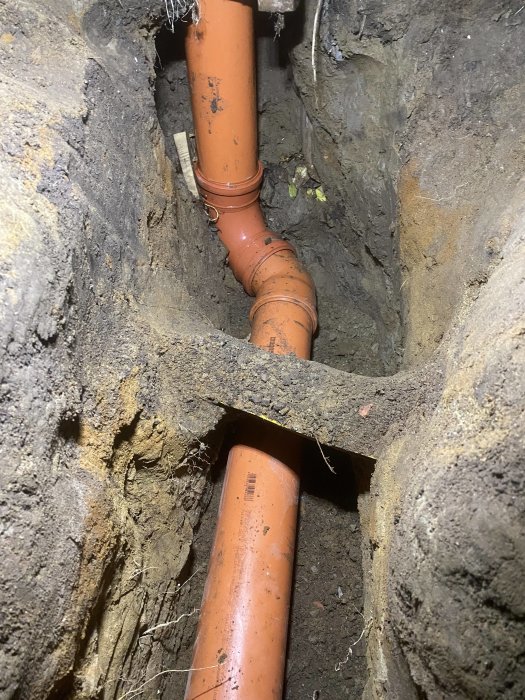 Orange dagvattenledningar anslutna i en grävd ränna, som sträcker sig under marken i en trång utrymme.