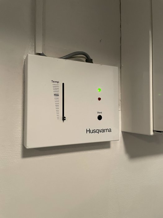 Husqvarna värmeregulator med temp- och vent-kontroller och grönt statusljus på vägg.