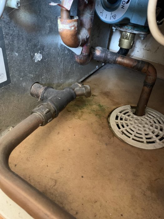 Avtappningsplats med fyrkantstapp på rör ovanför golvbrunn, potentiell korrosion synlig.