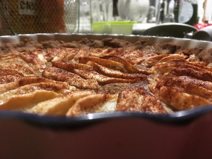 Nybakad äppelpaj med snittade äppelskivor och kanel i en pajform, sedd i närbild.