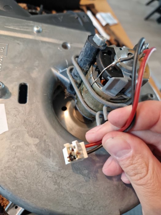 Person som håller i en elkontakt framför en öppnad elektrisk apparat.
