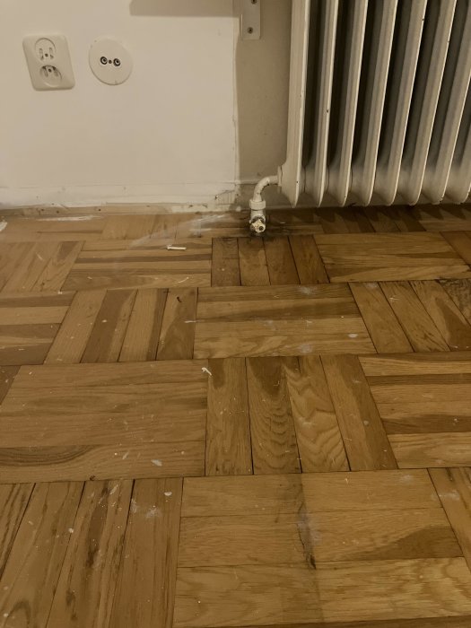 Vattenläckage vid värmeelement nära trägolv och vägg med synlig fuktskada och eluttag.