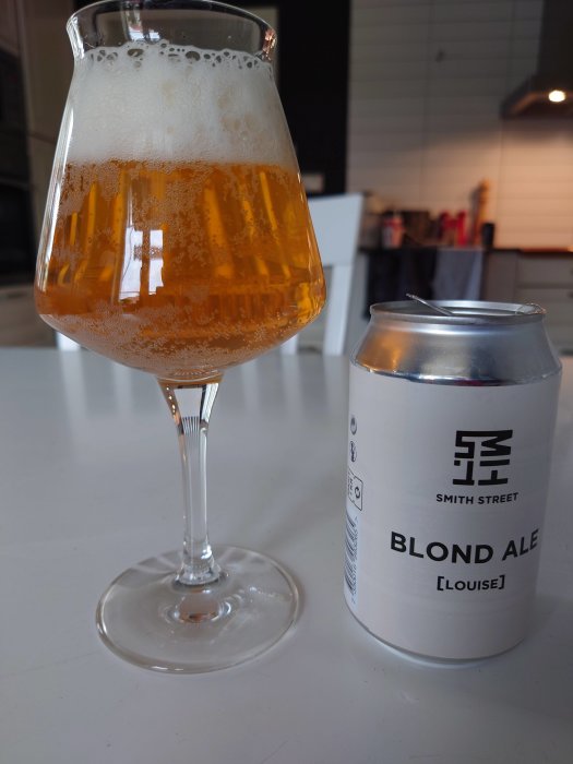 Ett glas fyllt med blond ale bredvid en ölburk märkt "Smith Street BLOND ALE [LOUISE]" på en köksbänk.