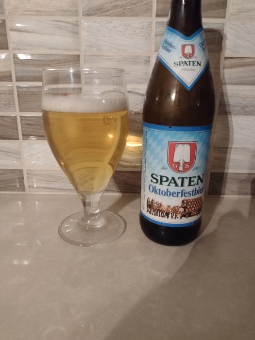 En flaska Spaten Oktoberfestbier bredvid ett glas med öl på en köksbänk.