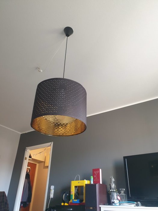 Nyinstallerad lampa med mönstrad skärm hänger från taket i ett rum med gråa väggar.