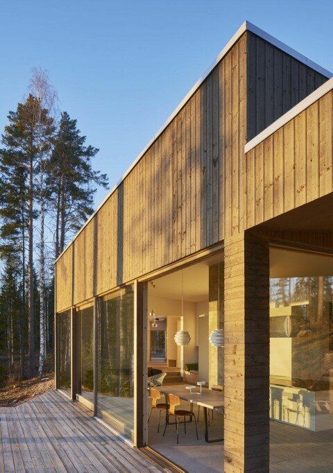 Modernt hus med träpanel och stora fönster som matchar takets lutning, dold entrédörr synlig vid närmare titt.