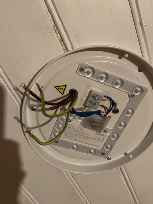 Öppen taklampa med synliga koppartrådar och anslutningsterminaler under installation.