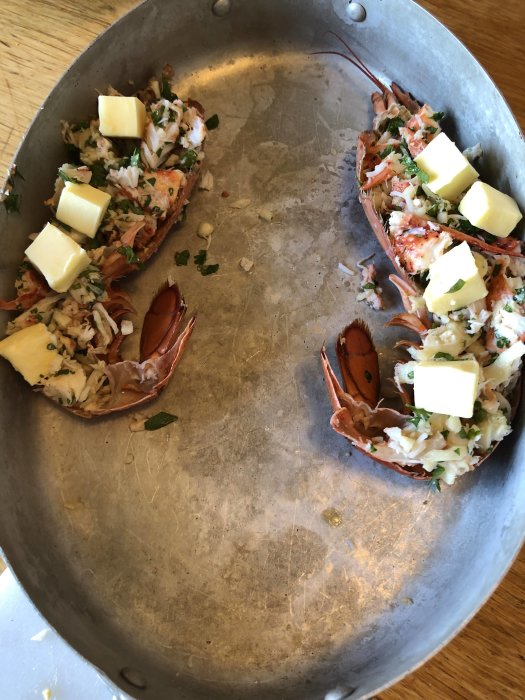 Halverad hummer med hackade örter och smörtärningar på ett metallfat.