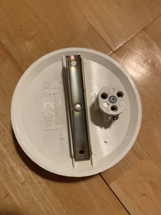 En gammal vit rund eldosas baksida med metallfäste och kontakter på ett trägolv.