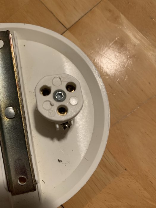 Närbild på en gammal vit elektrisk vägguttag framför ett parkettgolv.