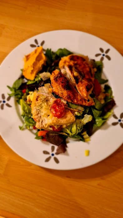 Kycklingfiléer toppade med mozzarella och körsbärstomater på en salladsbädd serverade med hummus.