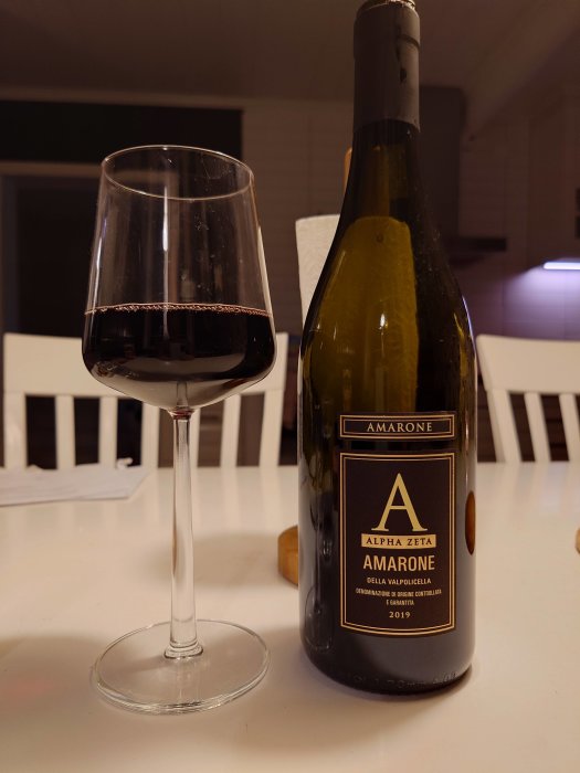 Rödvin i glas bredvid en flaska Amarone på ett vitt bord.