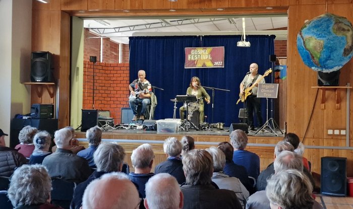 Publik tittar på en trio som uppträder på en scen under en gospel festival 2022.