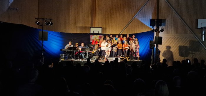 Publik framför scen med uppträdande band och kör i belyst aula under Gospel Revival.