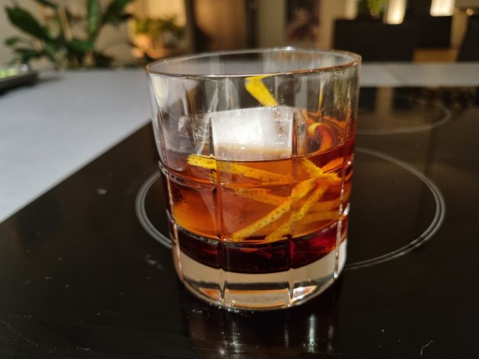 Glas med is och vermouth toppat med citronzest på ett bord.