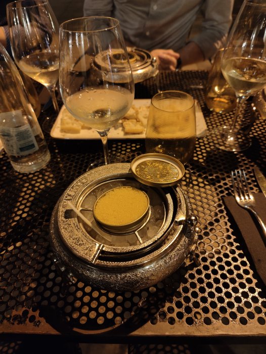 Lyxig servering av ål och anklever på en metallbricka, med vita vinglas och vattenflaskor i bakgrunden.