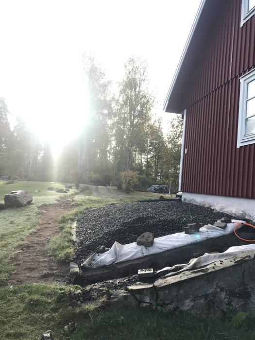 Nygrävd fiberkabelschakt vid husgrund med stenkant och spridda grönytor.