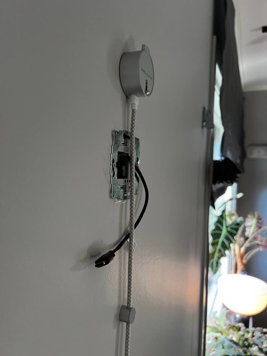 Väggmonterad USB-laddare med stickkontakt och utstickande USB-C-kabel bakom en högtalare med begränsat utrymme.