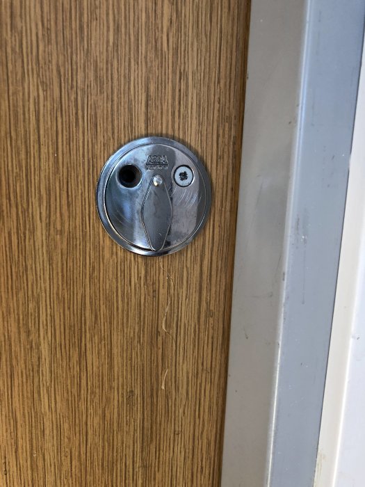 Ett befintligt låshus på en brun dörr, visar märket ASSA, saknar en skruv på vänster sida.