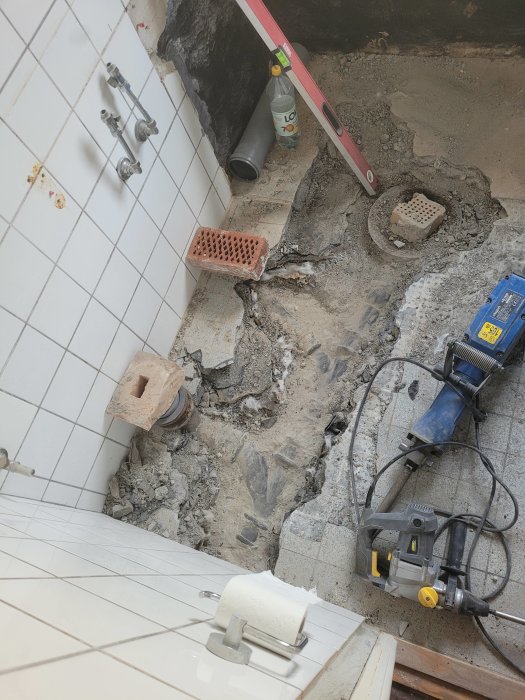 Renoveringsarbete i ett badrum med uppbruten golvkonstruktion, rör och verktyg synliga.