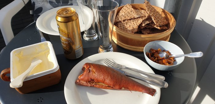 Rökt abborre på en tallrik, stekt kantareller i en skål, knäckebröd i en korg, smörburk och ölburk på ett bord.