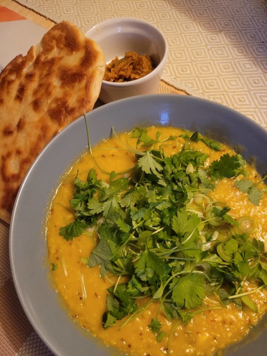 En tallrik med mung daal toppad med koriander, en bit naanbröd och en skål med kryddigt tillbehör.