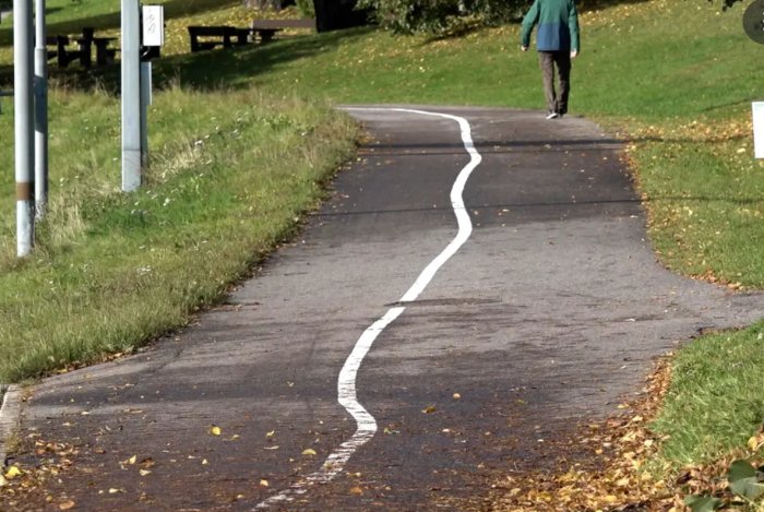 Väg med ojämnt målad, slingrig vit linje och en promenerande person i bakgrunden.