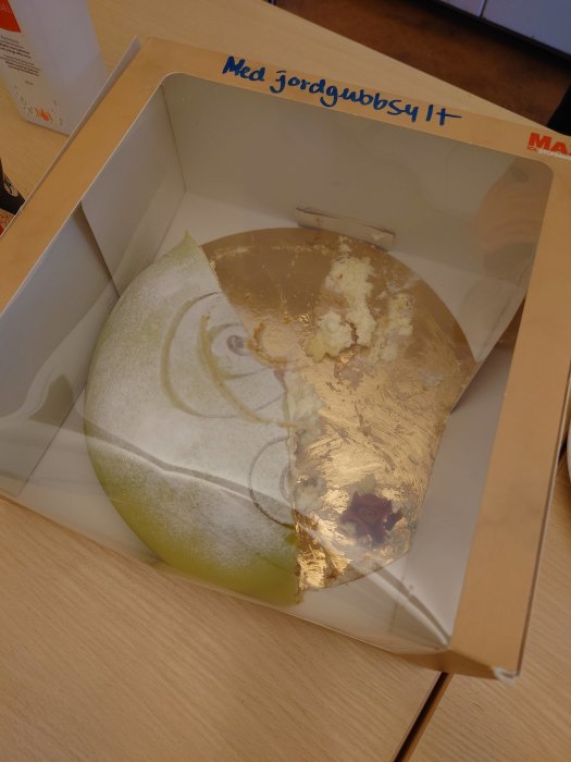 Halväten tårta med jordgubbssylt i en öppen kartong på ett bord.