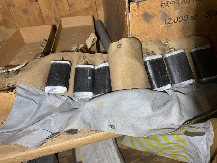 En verktygsbälte av linnetyg med flera svarta sylinddrar fästa på det, liggande på en träyta.