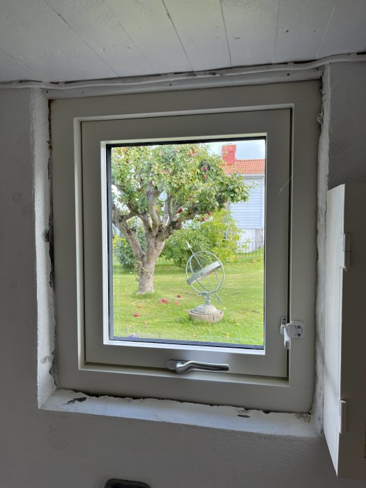 Nyinstallerat fönster med utsikt över trädgård, äppelträd och dekorativ vindflöjel.