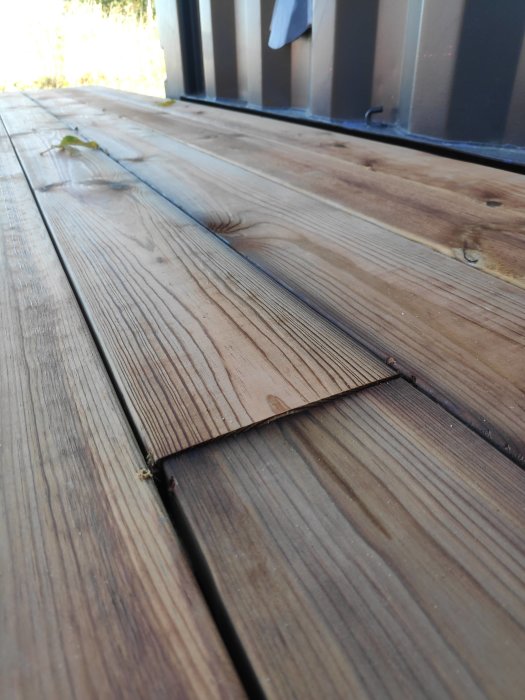 Trätrall med en uppböjd planka nära en altandörr, indikerar potentiellt byggfel eller skada.