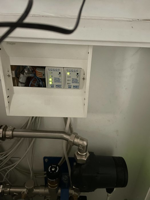 Elcentral med blinkande lampor bredvid rörledningar och en pump i ett tekniskt utrymme.