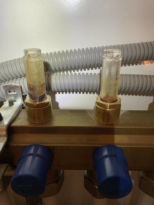 Vattenrör med isolering och två genomskinliga vattenmätare eller nivåindikatorer monterade på en träplatta.