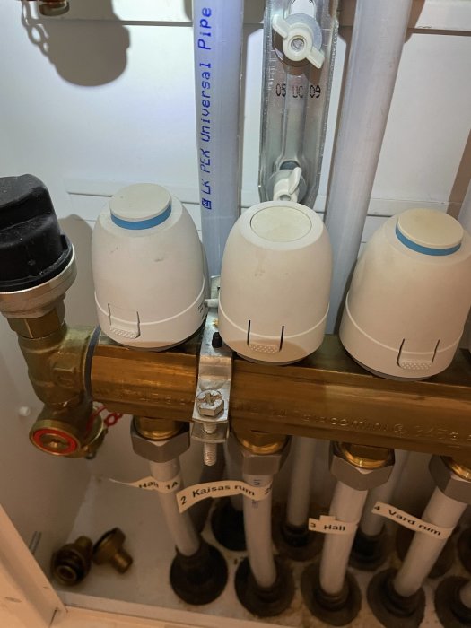 Värmeinstallation med termostatventiler och märkta rör för olika rum.