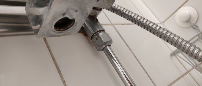 Rostig anslutning mellan en duschslang och duschmunstycket mot kakelvägg.