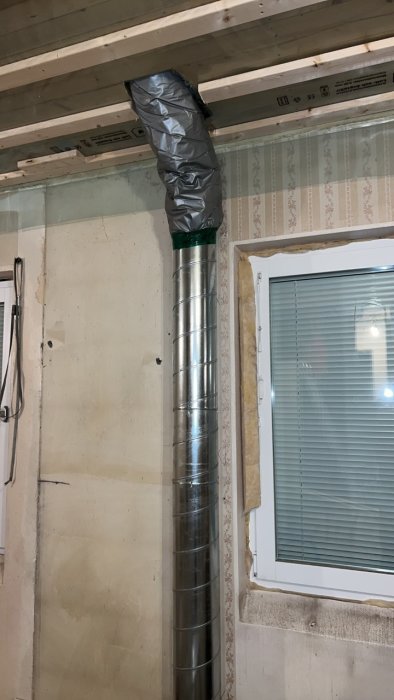 Nyinstallerat ventilationsrör i ett rum under renovering med tejpade skarvar och isolering.