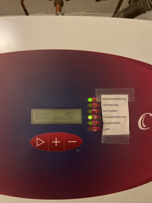 Display och kontrollpanel på värmepump med indikatorlampor och klisterlapp för manöverindikering.