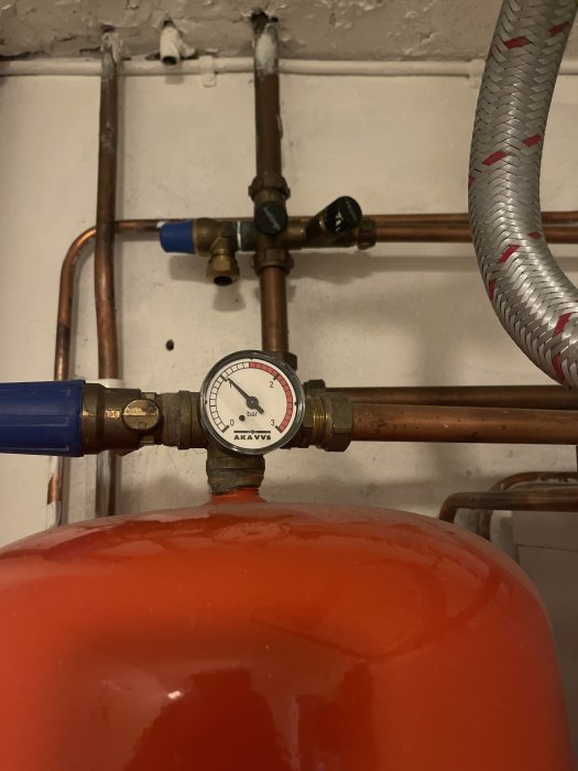 Manometer monterad på röd expansionskärl med kopparledningar och avstängningsventiler i bakgrunden.