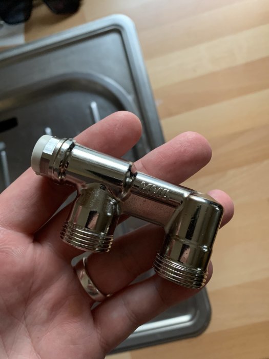 Hand håller ett nytt metall rör med sidoluftning framför en diskho.