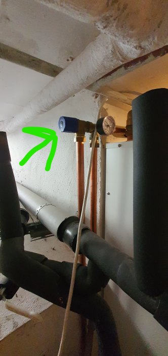 VVS-installation i källare med rör, manometer och isolering markerad med grön pil.