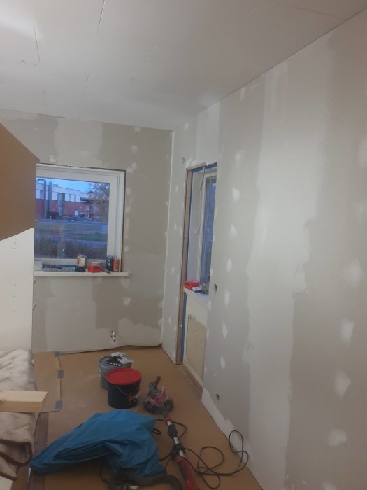 Rum under renovering med nyligen uppsatta gipsskivor och spacklade väggar redo för målning.