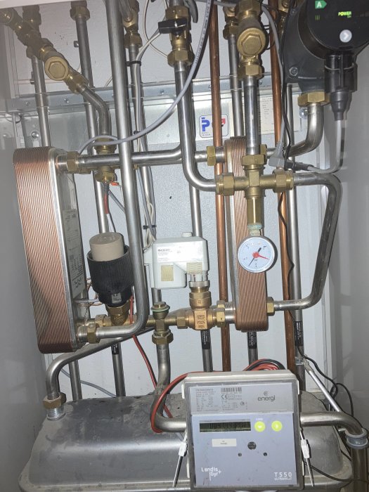 Värmesystem med kopparledningar, ventiler, mätare och energimätare på en vägg.