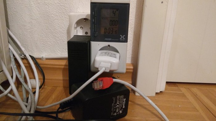 Energimätare och adaptrar inkopplade i eluttag med kablar på golv.