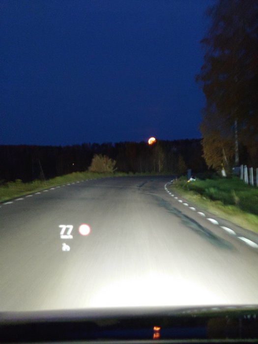 Oskarpt foto taget inifrån en bil som visar en mörk väg och en suddig gatlykta på kvällen.